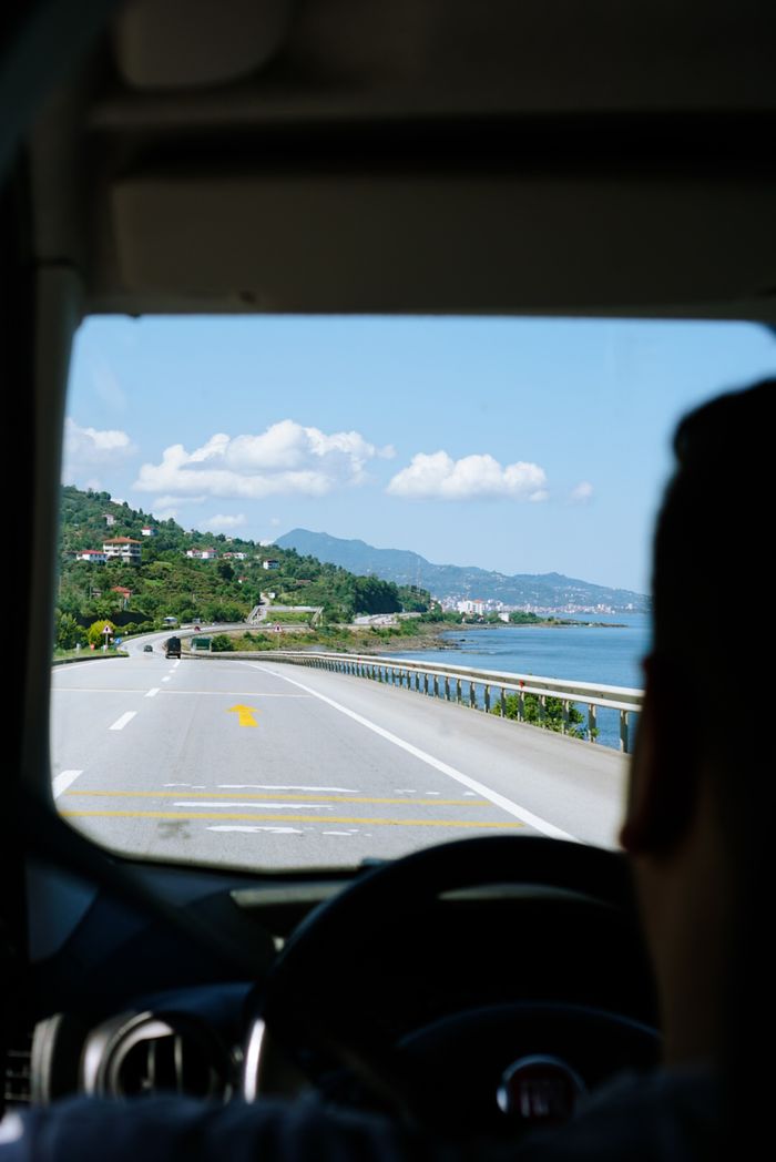 View from a car driving along a scenic coastal road with mountains and sea view.