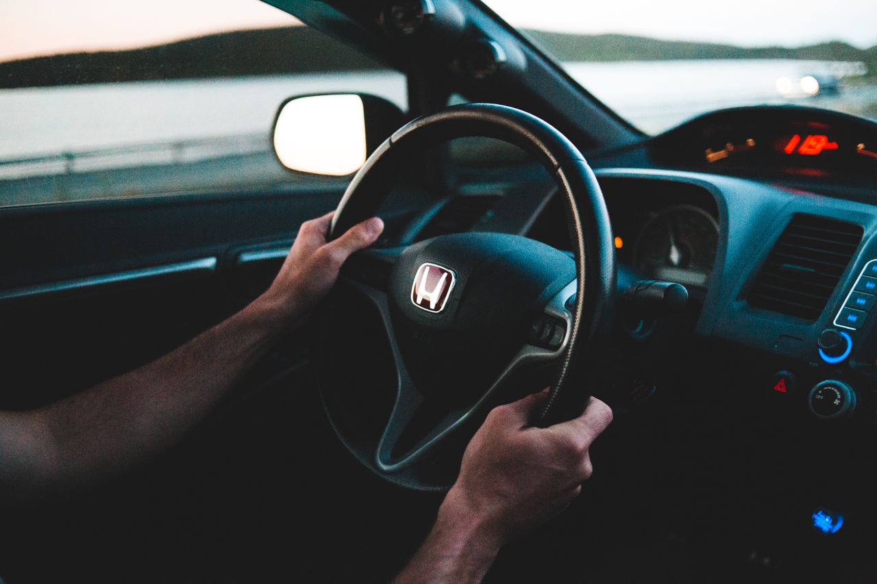 Crop unrecognizable man driving contemporary auto near lake under white sky in evening